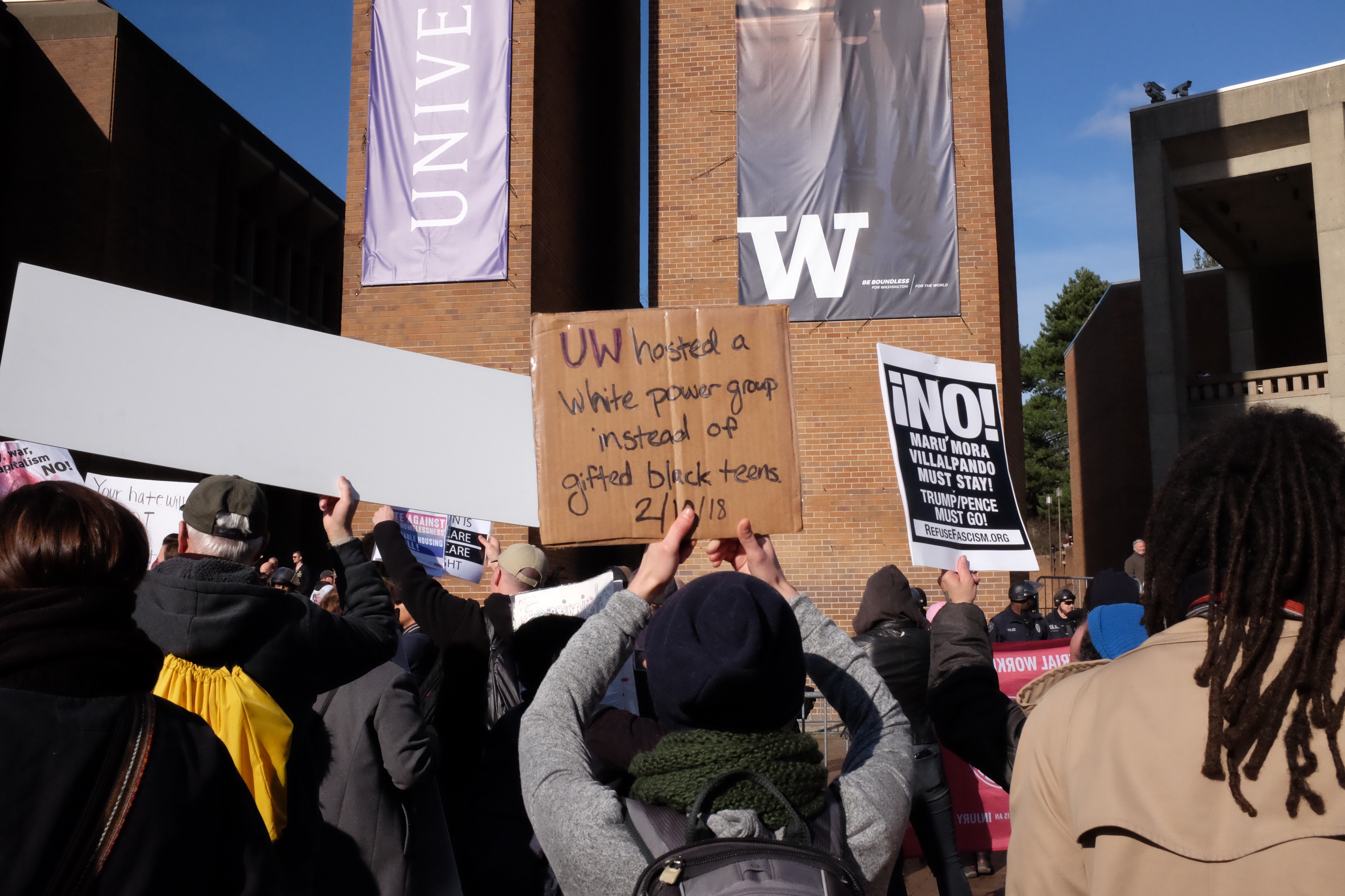 A counter-protester holds a sign that reads "UW hosted a white power group instead of gifted black teens 2/10/18".
