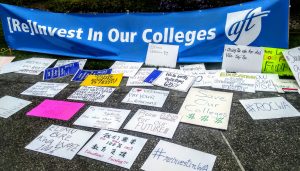 collection of protest signage in front of Reinvest in Our Colleges sign